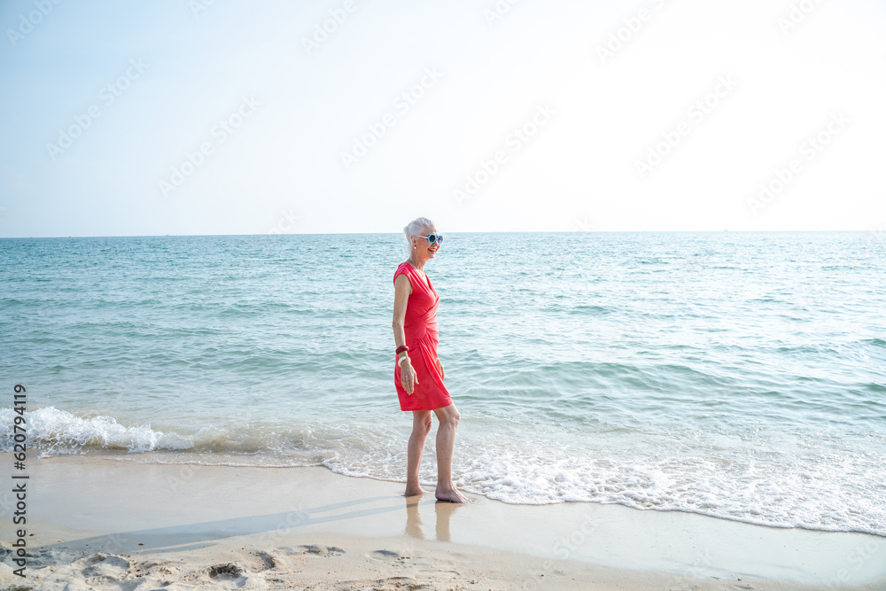 Happy retired woman relaxing on sand at the beach.