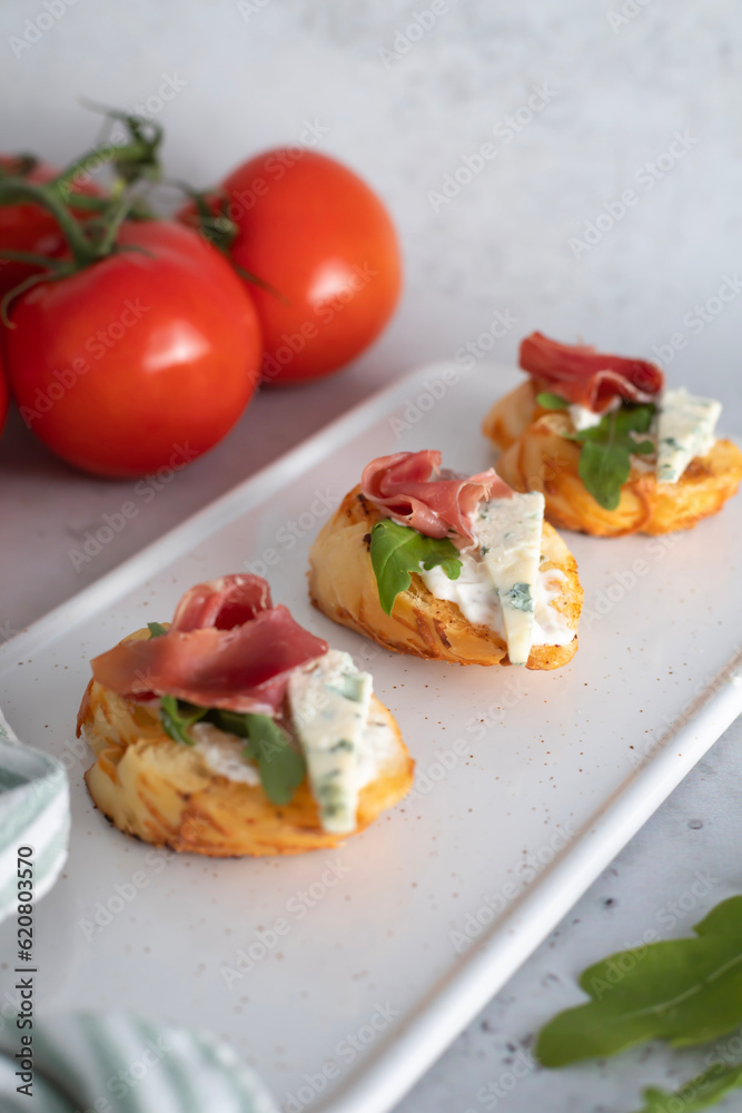 On the kitchen table is a board with fresh bruschetta with ham and cheese. Along with tomatoes and greens