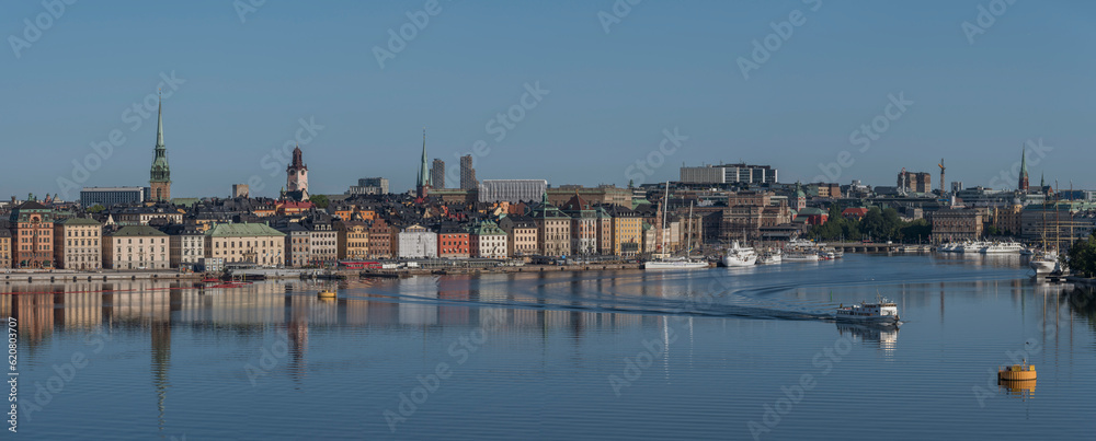 Panorama, view over the bay Strömmen, the old town Gamla Stan, boats marooned at piers, archipelago ferry leaving, water mirror reflections, a sunny summer morning in Stockholm