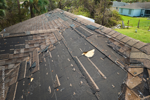 Damaged house roof with missing shingles after hurricane Ian in Florida. Consequences of natural disaster