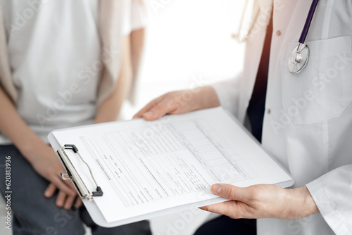 Doctor and child patient. The physician is holding clipboard with medication history records form near a boy. The concept of ideal health in medicine