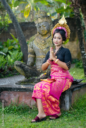 Woman praying in front of a Buddha statue in a traditionally costume and a crown in hair