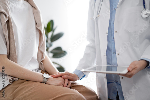Doctor and patient discussing health exam results. Friendly physician reassuring a young woman by one hand while keeping tablet computer in another. Medicine concept