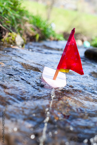 Toy boat with red sail in the river. Spielzeugboot mit rotem Segel im Bach.