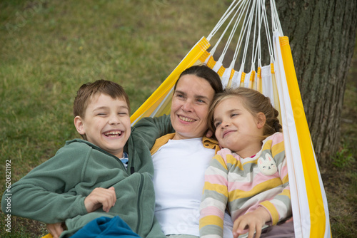 mom and Two kids swing in a hammock in a summer park or garden. Concept of friendly family.