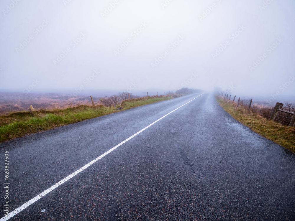 Asphalt road and fields in country side in a fog. Dangerous driving conditions with low visibility and wet road surface. Mist over wild nature. Asphalt road and fields in country side in a fog. Dangerous driving conditions with low visibility and wet road surface. Mist over wild nature.