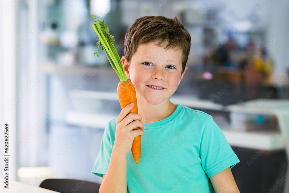Smiling boy with carrot against blurred kitchen Smiling boy with carrot against blurred kitchen