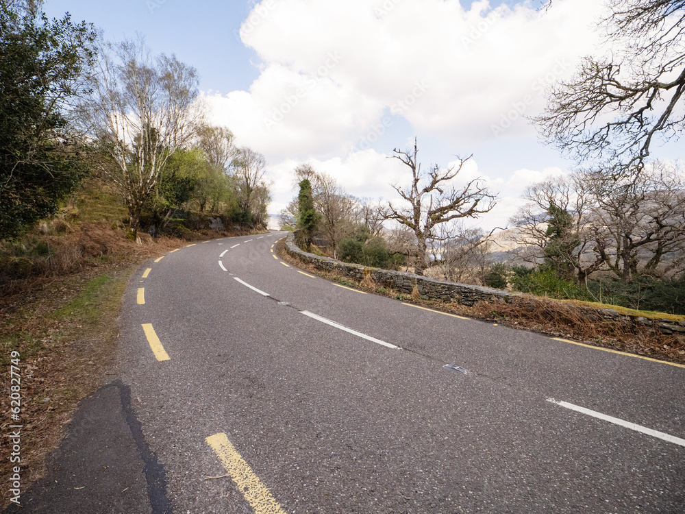Fototapeta premium Small asphalt road with stunning nature scenery in county Kerry, Ireland. Amazing Irish landscape by a popular travel rout for tourist. Warm sunny day cloudy sky. Sightseeing and explore wild scenery