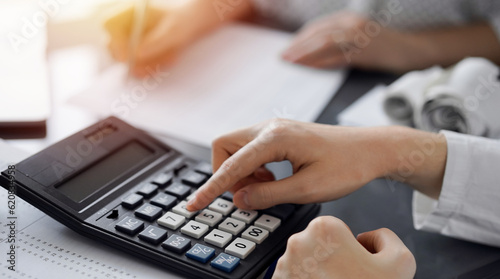 Woman accountant using a calculator and laptop computer while counting taxes for a client. Business audit and finance concepts