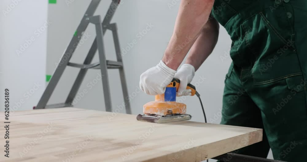 Man holds belt sander on wooden floor or tabletop sanding surface. Preparing wood for painting Man holds belt sander on wooden floor or tabletop sanding surface. Preparing wood for painting