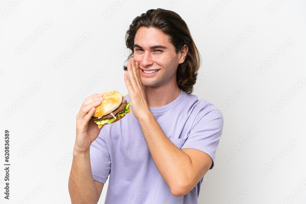Young handsome man holding a burger isolated on white background whispering something