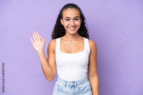 Young woman isolated on purple background saluting with hand with happy expression
