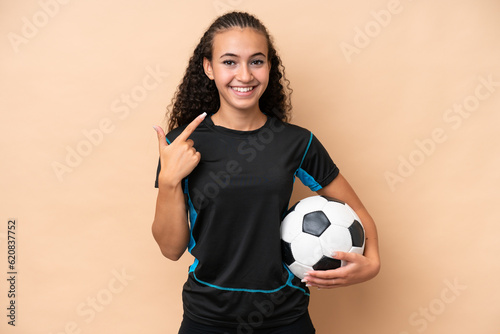 Young football player woman isolated on beige background giving a thumbs up gesture © luismolinero
