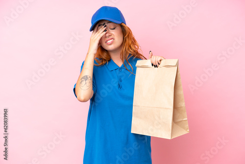 Young caucasian woman taking a bag of takeaway food isolated on pink background with tired and sick expression