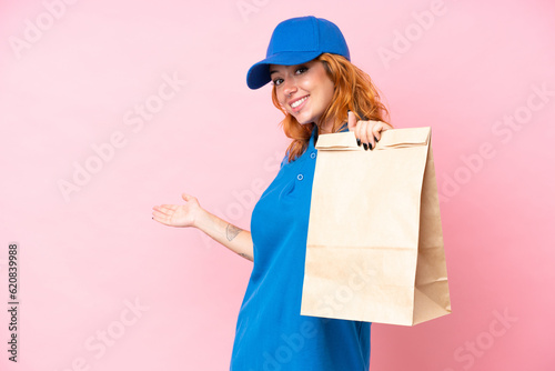 Young caucasian woman taking a bag of takeaway food isolated on pink background extending hands to the side for inviting to come