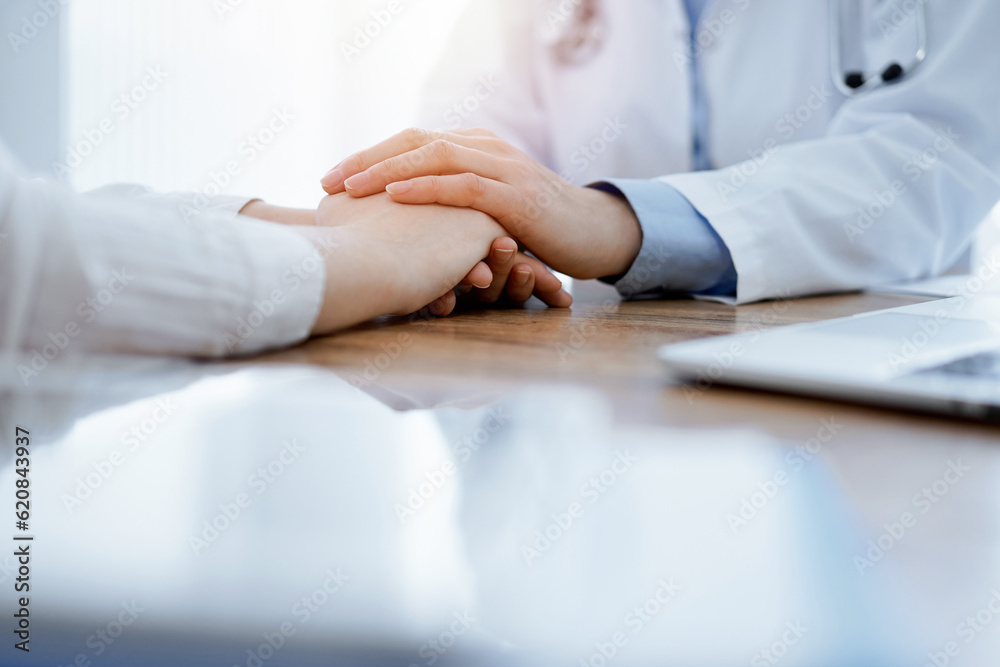 Doctor and patient sitting at the wooden table in clinic. Female physician's hands reassuring woman. Medicine concept Doctor and patient sitting at the wooden table in clinic. Female physician's hands reassuring woman. Medicine concept