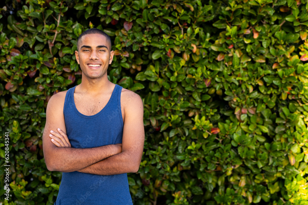 Portrait of happy biracial man standing against hedge smiling in sunny garden, copy space Portrait of happy biracial man standing against hedge smiling in sunny garden, copy space