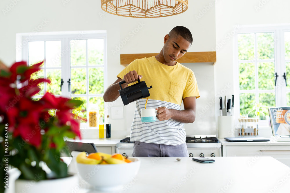 Biracial man pouring cup of coffee in sunny kitchen Biracial man pouring cup of coffee in sunny kitchen