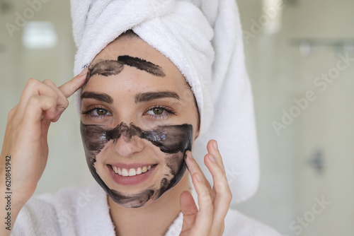 Portrait of happy caucasian woman with towel on head making mask on face in bathroom, copy space photo