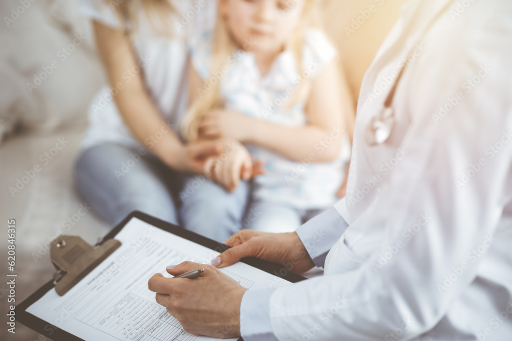 Doctor and patient. Pediatrician using clipboard while examining little girl with her mother at home. Sick and unhappy child at medical exam