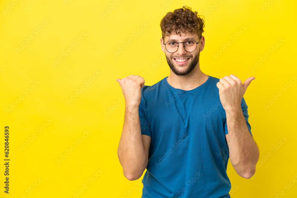Young handsome caucasian man isolated on yellow background with thumbs up gesture and smiling Young handsome caucasian man isolated on yellow background with thumbs up gesture and smiling