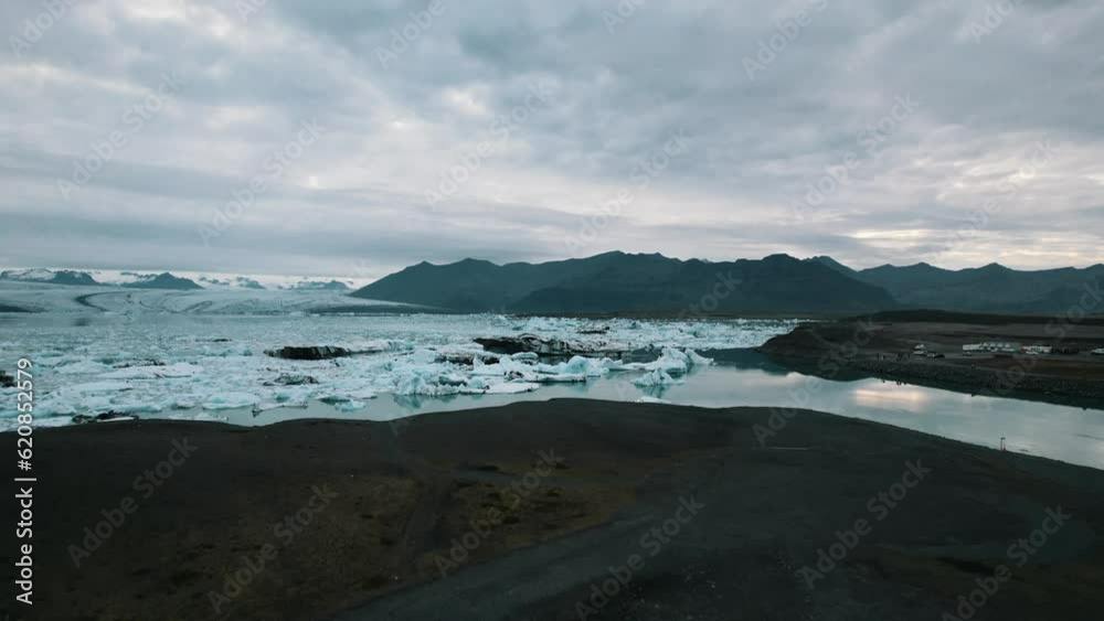 Panoramic view of Iceberg drifting on the glacier water surface, Melting glaciers due to global warming, Mountains under an overcast sky, Iceland, Slow motion drone shot Panoramic view of Iceberg drifting on the glacier water surface, Melting glaciers due to global warming, Mountains under an overcast sky, Iceland, Slow motion drone shot