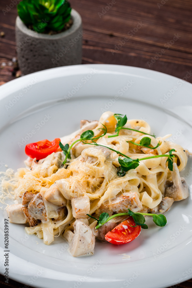 Linguini pasta with chicken fillet, mushrooms, cheese, cream sauce, tomatoes and herbs, Italian dinner.