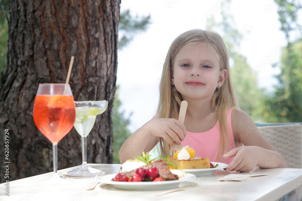Cheerful little girl eating cake at the outdoor cafe Cheerful little girl eating cake at the outdoor cafe