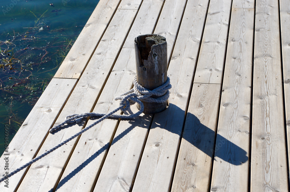 Fototapeta premium Wooden pier with a wooden pole bollard and tied ropes.