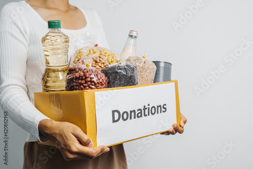 Female volunteer hands holding food in donation box, grocery products. at charitable foundation. Working at food bank, help for poor families, migrants, refugees concept.