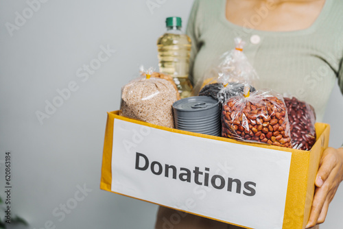 Female volunteer hands holding food in donation box, grocery products. at charitable foundation. Working at food bank, help for poor families, migrants, refugees concept.