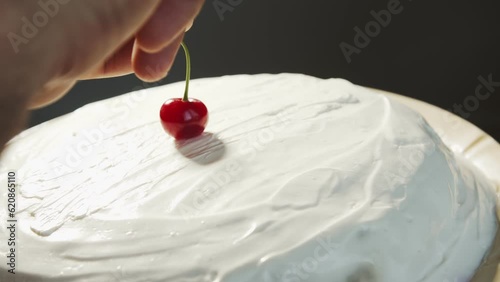 Cherry on the cake. Apotheosis. Finish. A hand puts a red cherry on a homemade white cake that rotates at an angle photo