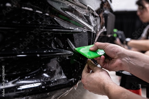 Obraz na płótnie Car detailing studio employee, a wrapper, is protecting the bumper of a black car with a colorless protective PPF film. The PPF film protects the paint from scratches and damage. w salonie