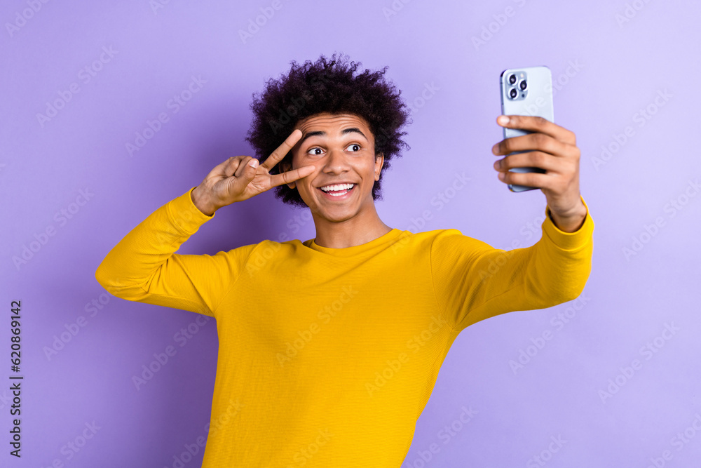 Portrait of funky excited person hold smart phone take selfie show v-sign near eye isolated on purple color background Portrait of funky excited person hold smart phone take selfie show v-sign near eye isolated on purple color background