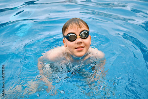 Smiling boy portrait in swimming goggles, Child swim in the pool, sunbathes, swimming in hot summer day. Relax, Travel, Holidays 