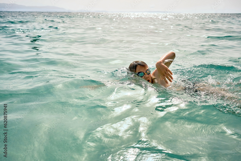 Happy boy in swimming goggles swim in the sea looking at view enjoying summer vacation. Togetherness Friendly concept
