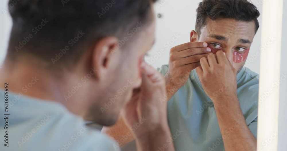 Biracial man looking in mirror applying under eye masks in bathroom, slow motion Biracial man looking in mirror applying under eye masks in bathroom, slow motion