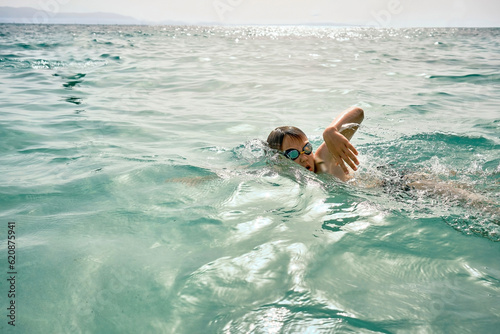 Happy boy in swimming goggles swim in the sea looking at view enjoying summer vacation. Togetherness Friendly concept 
