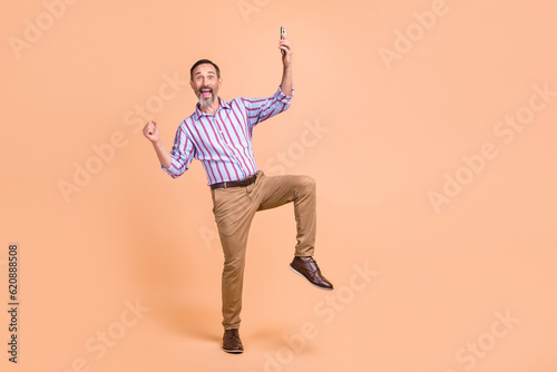 Full length portrait of delighted crazy man hold smart phone raise fist achievement empty space isolated on beige color background