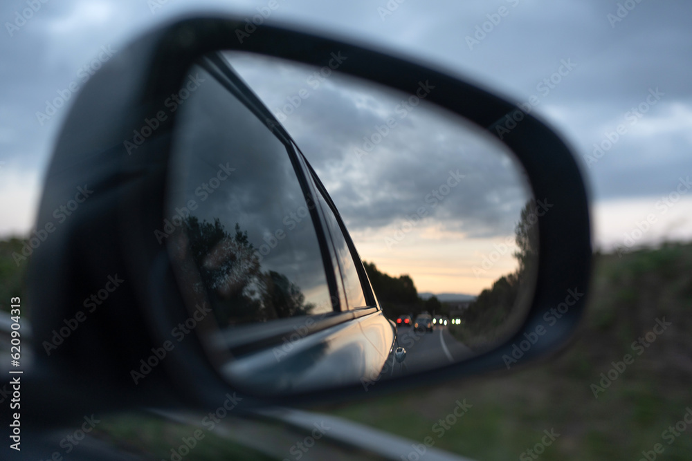 rear-view mirror with sunset and cars with their lights behind them