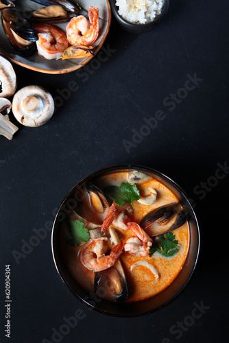 Tom Yam soup with coconut milk with shrimp, squid, mussels and mushrooms. Vertical photo on a dark backgroundFlat lay. Top view. Copy space.. photo