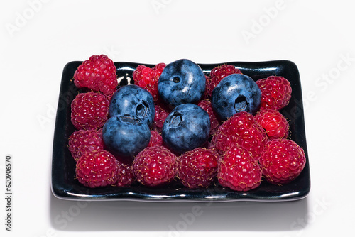 Sweet fresh organic raspberries and blueberries in a black plate on a white background