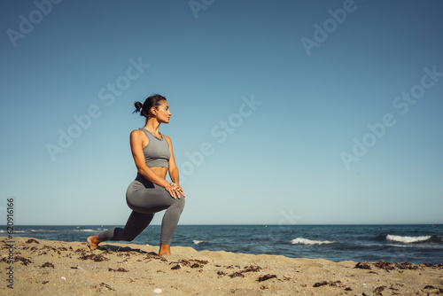 a beautiful brunette girl in gray leggings is engaged in fitness on the sand against the background of the sea
