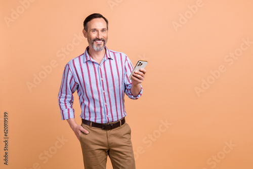 Portrait of handsome optimistic person with beard striped shirt hold smartphone hand in pocket isolated on pastel color background