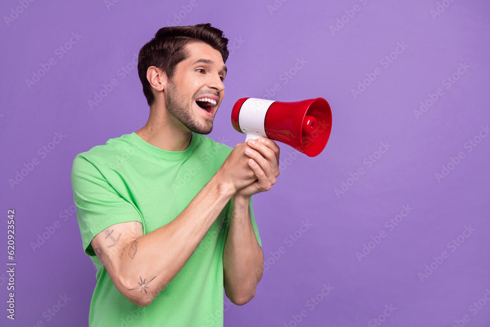 Portrait of optimistic guy with bristle wear green t-shirt shout in loudspeaker look empty space isolated on violet color background