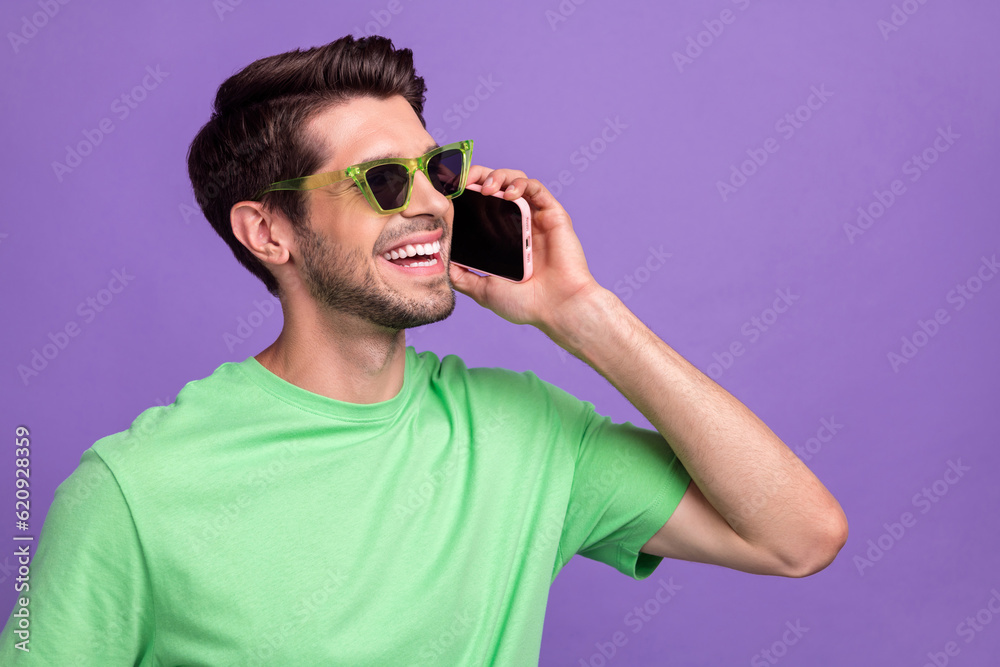 Portrait of carefree cool guy with bristle wear green t-shirt talk on smartphone look empty space isolated on violet color background Portrait of carefree cool guy with bristle wear green t-shirt talk on smartphone look empty space isolated on violet color background