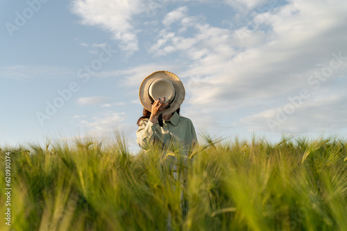 Woman standing in a field covering her face with a straw hat, Belarus photo