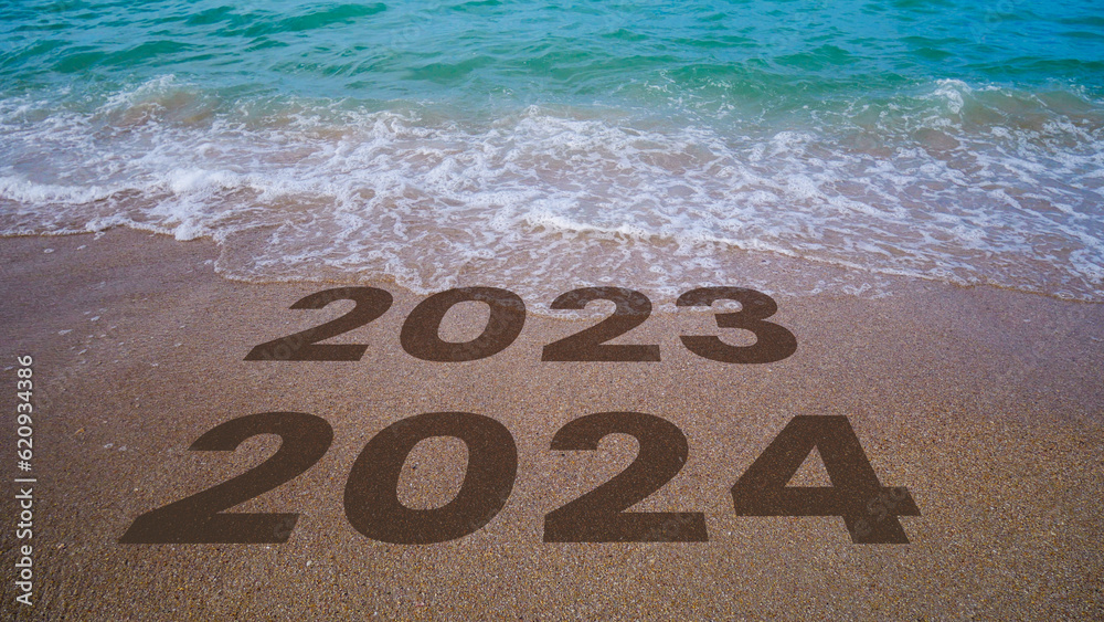 The waves erase 2023 to 2024 written in the sand by the beach. 2024