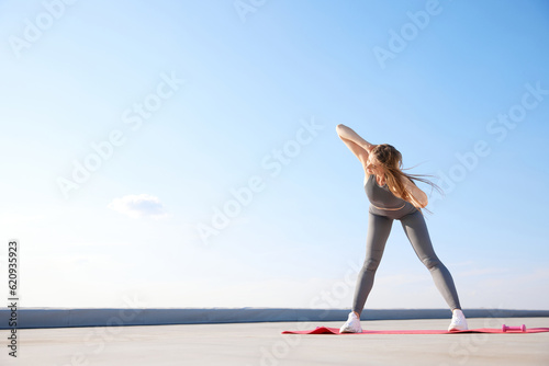 Warming up exercises. Young woman with slim, sportive body training, doing stretching on warm summer morning outdoors
