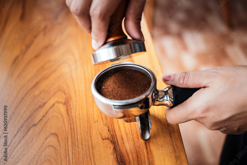 Close-up of hand Barista cafe making coffee with manual presses ground coffee using tamper on the wooden counter bar at the coffee shop Close-up of hand Barista cafe making coffee with manual presses ground coffee using tamper on the wooden counter bar at the coffee shop